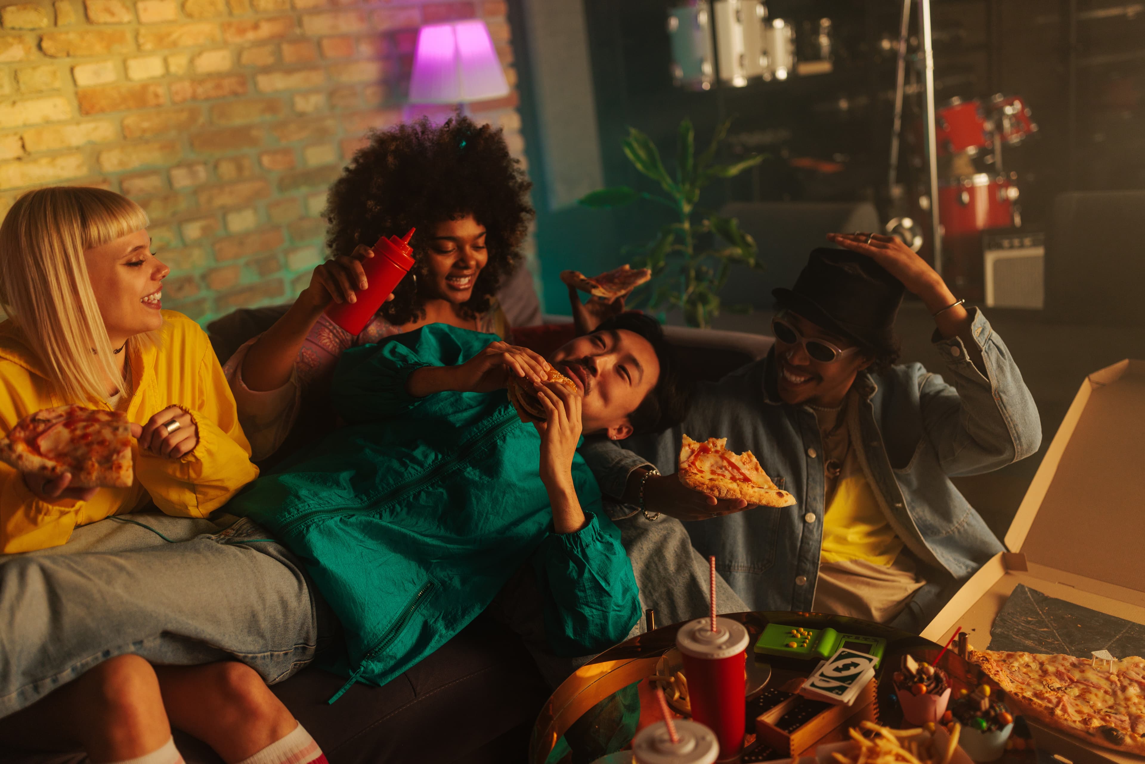 Four friends eating pizza in a dim lamplit living room